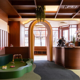 Modern cafe or kid-friendly play area with wooden finishes, a curved archway, and a green soft play mat with toys in the foreground.