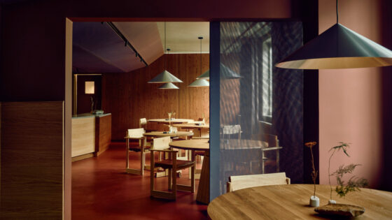 Cozy modern cafe with round wooden tables, minimalist chairs, warm pendant lighting, and wood-paneled walls.
