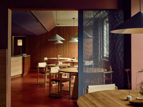Cozy modern cafe with round wooden tables, minimalist chairs, warm pendant lighting, and wood-paneled walls.