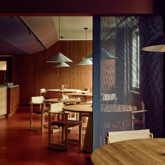 Cozy modern cafe with round wooden tables, minimalist chairs, warm pendant lighting, and wood-paneled walls.