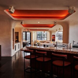 Modern bar interior with red illuminated ceiling panels, curved white walls, a dark wooden bar with red stools, and large windows in the background.