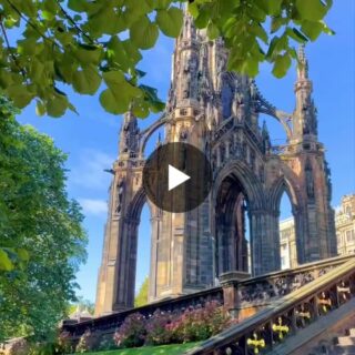 Gothic ruin with ornate arches framed by green leaves and a blue sky, stairs with decorative railing in the foreground.