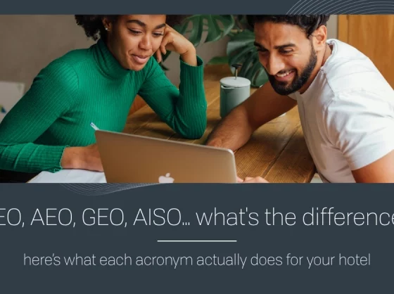 Two colleagues lean over a laptop at a wooden table, reviewing a hotel marketing banner that asks, 'SEO, AEO, GEO, AISO… what’s the difference?' with a subtitle about what each acronym does for your hotel.