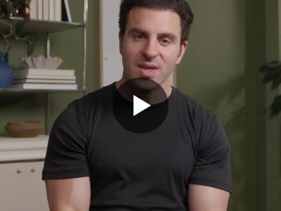 Video thumbnail: man in a black T-shirt sits in a green-walled room, speaking to the viewer with a play button overlay.
