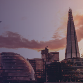 Silhouette of London's skyline at sunset, featuring The Shard and rounded city buildings against a pink‑orange sky with a few birds in flight.