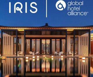 Nighttime exterior of a modern hotel with a reflecting pool and warm lighting; IRIS and Global Hotel Alliance logos sit above the entrance.
