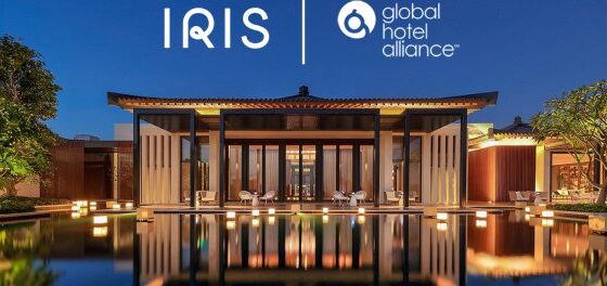 Nighttime exterior of a modern hotel with a reflecting pool and warm lighting; IRIS and Global Hotel Alliance logos sit above the entrance.