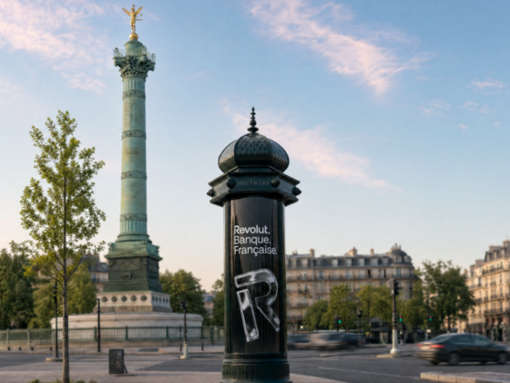 Paris street scene with the July Column monument and a black cylindrical ad column reading 'Revolut. Banque Française'. The sky is blue and light clouds above. (informative)