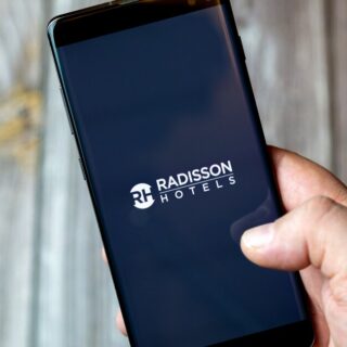 Smartphone in hand displaying the Radisson Hotels logo on screen.