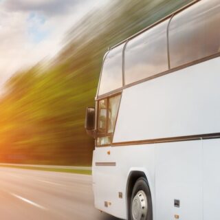 White passenger bus speeding along a multi-lane highway at sunset with motion blur.