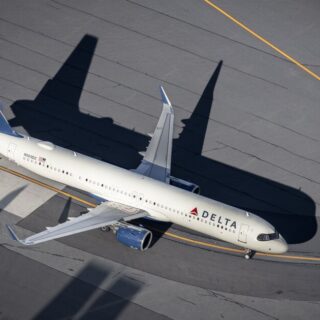 Delta Airlines jet taxiing on the gray tarmac with its shadow stretched across the ground