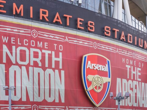 Exterior of Emirates Stadium with a large red banner reading 'Welcome to North London' and the Arsenal crest in the center.