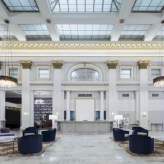 Luxurious hotel lobby with marble floor, white columns, central reception desk, skylight ceiling, crystal chandeliers, and purple seating.