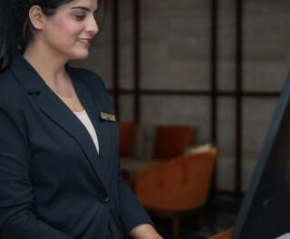 Front desk receptionist in a dark blazer smiling while using a computer at a workstation