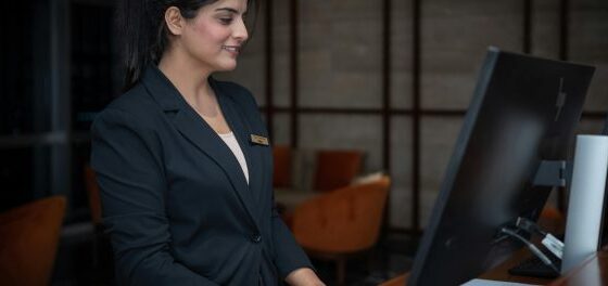 Front desk receptionist in a dark blazer smiling while using a computer at a workstation