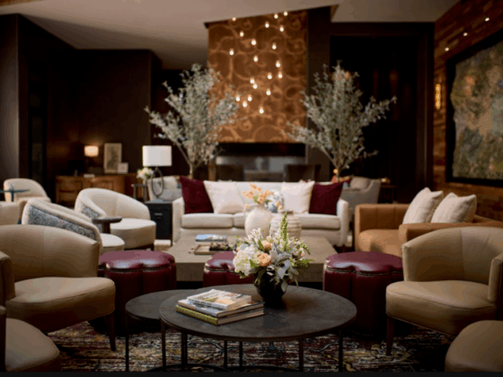 Luxurious hotel lobby lounge with beige chairs, burgundy ottomans, and a central round coffee table with a floral arrangement.