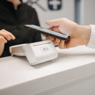 Person uses a smartphone to pay by tapping it on a contactless payment terminal at a white counter