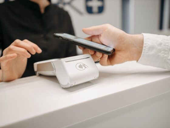 Person uses a smartphone to pay by tapping it on a contactless payment terminal at a white counter