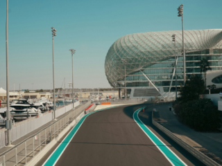 Modern waterfront race track leading to a futuristic glass building with a lattice dome.