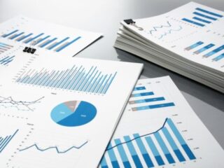 Desk with multiple printed reports showing blue bar charts, line graphs, and a pie chart clipped with binder clips.