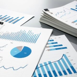 Desk with multiple printed reports showing blue bar charts, line graphs, and a pie chart clipped with binder clips.