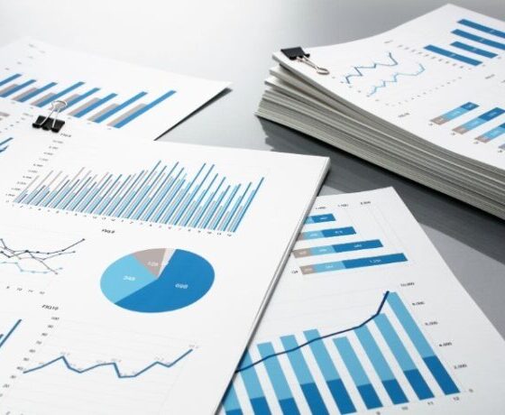 Desk with multiple printed reports showing blue bar charts, line graphs, and a pie chart clipped with binder clips.
