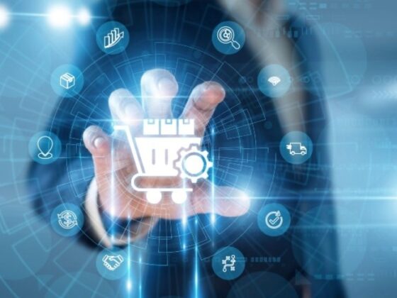 Person in a suit touches a glowing holographic shopping cart with gears, surrounded by digital icons representing e-commerce.