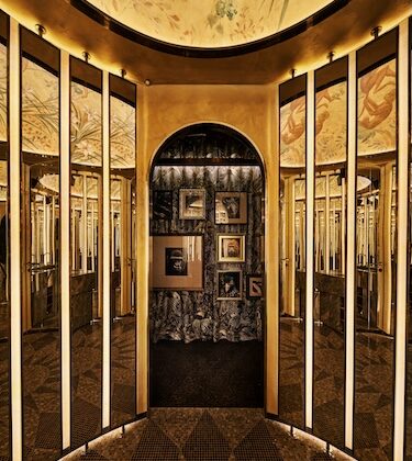 Gold-toned mirrored hallway leading to a small gallery with framed pictures on a dark wall at the end.