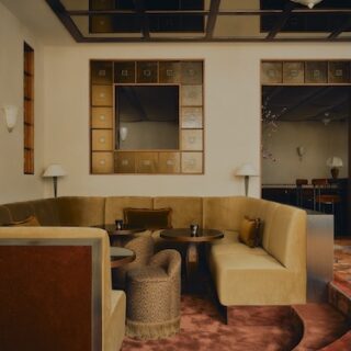 Cozy hotel lounge with beige sectional seating around round tables, patterned red carpet, and wall-mounted mirrors.