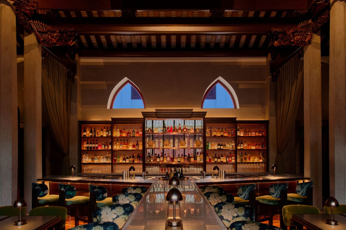 Elegant bar interior with backlit liquor shelves, bottles lined up, and two blue arched windows in the background.