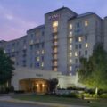 Hyatt hotel exterior at dusk, a multi-story beige building with lit windows and a welcoming entrance canopy.