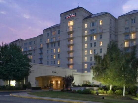 Hyatt hotel exterior at dusk, a multi-story beige building with lit windows and a welcoming entrance canopy.