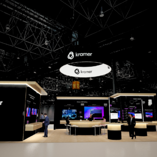 Kramer trade show booth with black panels, circular hanging logo, and visitors at counters under a bright ceiling rigging.