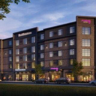 Exterior view of a modern brick hotel at dusk with Moxy signage and street-level storefronts