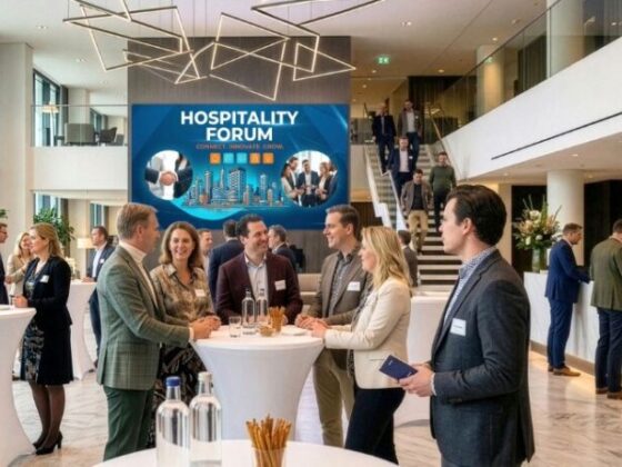 Professionals networking at round high tables in a bright modern lobby with a blue Hospitality Forum banner in the background.