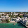 Aerial view of a tropical coastal town with waterfront resorts and a marina along clear blue-green water with palm trees.