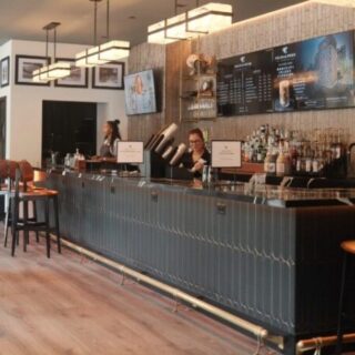 Long bar with two bartenders serving behind a tiled counter, menu boards above and stools along the bar