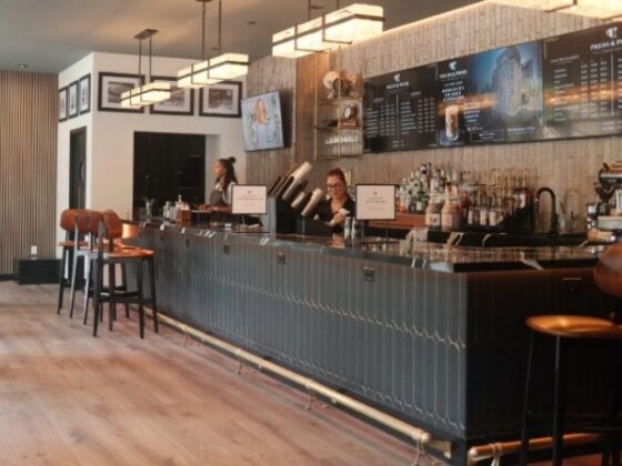 Long bar with two bartenders serving behind a tiled counter, menu boards above and stools along the bar
