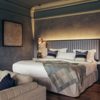 Cozy modern bedroom with a gray wall, upholstered headboard, and warm pendant lights above nightstands.