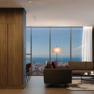 Modern living room with brown sofa, coffee table, floor lamp, and floor-to-ceiling windows overlooking a city and the ocean.