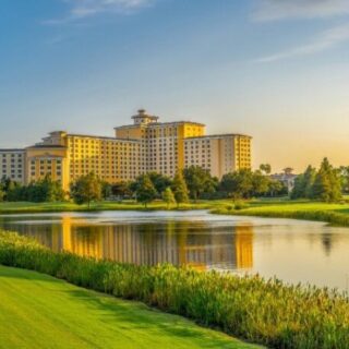 Resort-style hotel complex near a lake with manicured golf greens in the foreground at sunset