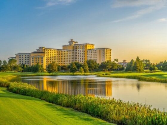 Resort-style hotel complex near a lake with manicured golf greens in the foreground at sunset
