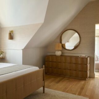 Cozy neutral bedroom with a sloped ceiling, bed, and wooden dresser with a round mirror against beige walls.