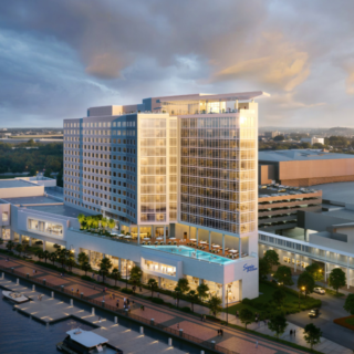 A modern waterfront hotel complex with a tall glass facade, outdoor pool, and marina along a promenade at dusk/light.