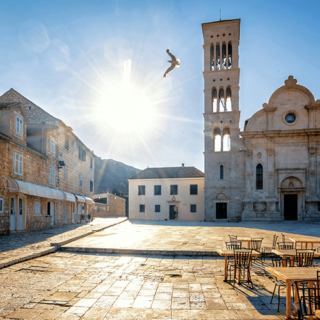 Sunlit historic square with stone buildings, a church, and outdoor café tables; a bird flies near the sun.
