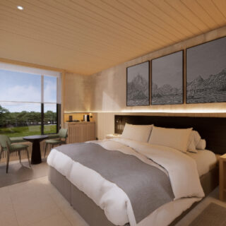 Hotel room with a king bed, gray accent blanket, seating area by the window, and triptych mountain art above the headboard.