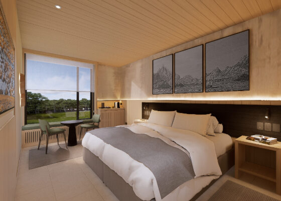 Hotel room with a king bed, gray accent blanket, seating area by the window, and triptych mountain art above the headboard.
