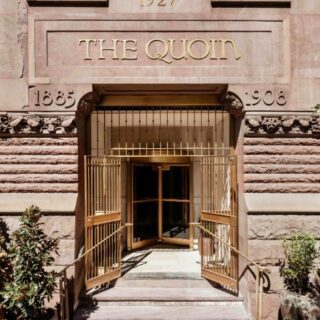 Entrance to The Quoin, a sandstone building with open gold-tone gates and potted plants along the doorway.