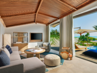 Luxurious living room with a wooden vaulted ceiling opening to a beachside view and pool outside