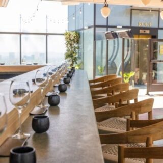Rooftop dining bar with a long counter set for service, wine glasses lined up and sunlight streaming in.